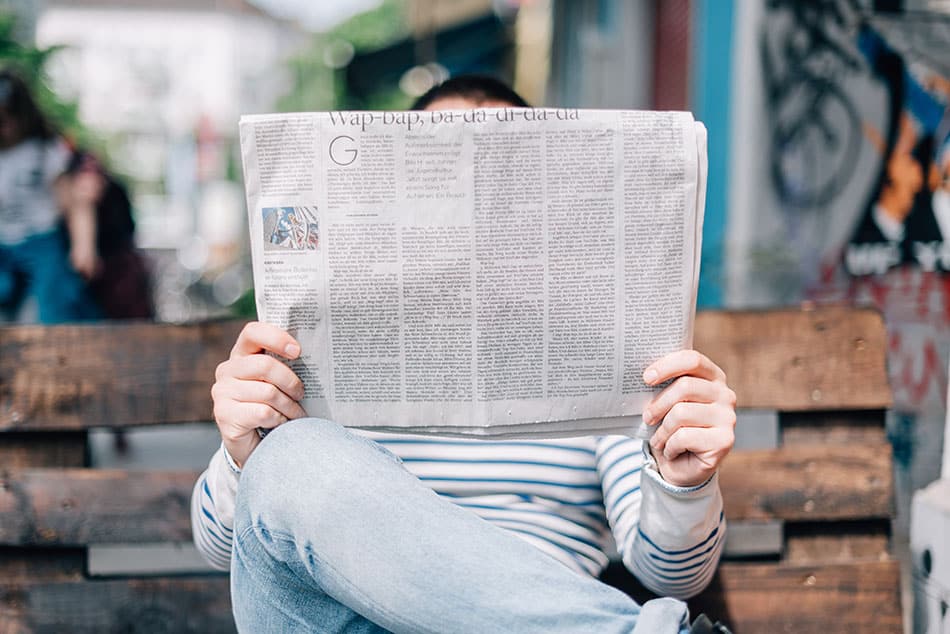 Eine Person sitzt auf einer Bank und liest eine Zeitung
